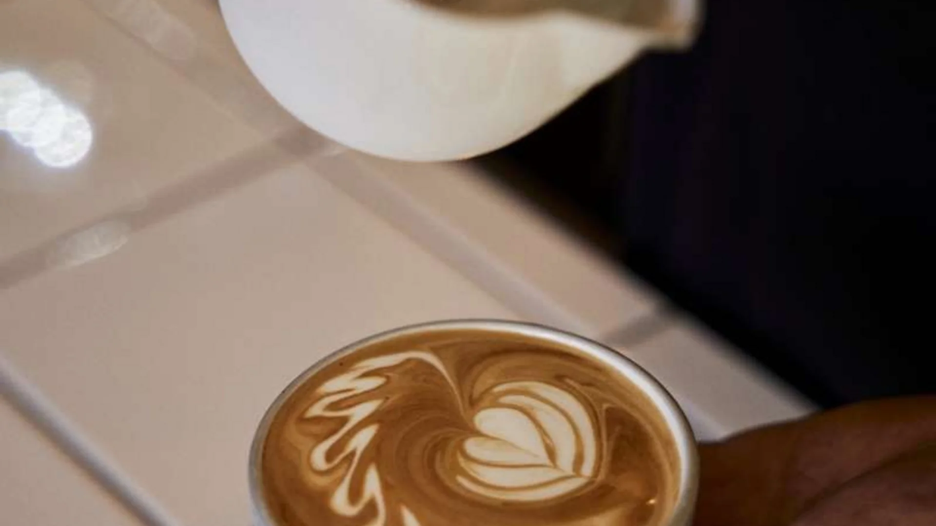 Latte Art in einer kleinen weißen Tasse auf einer Hand gehalten