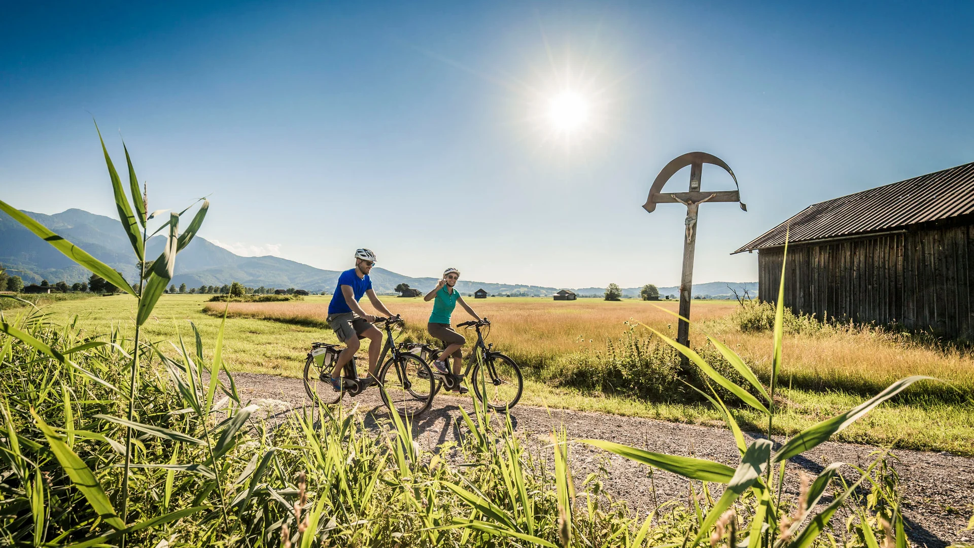 Zwei Radfahrer auf Landweg bei sonnigem Wetter vor Berglandschaft