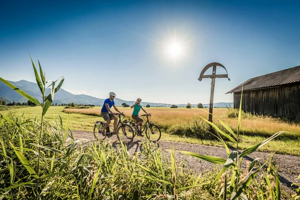 Duitsland © Tourist Information Kochel am See - Thomas Kujat Twee fietsers op landweg bij zonnig weer met bergen op de achtergrond