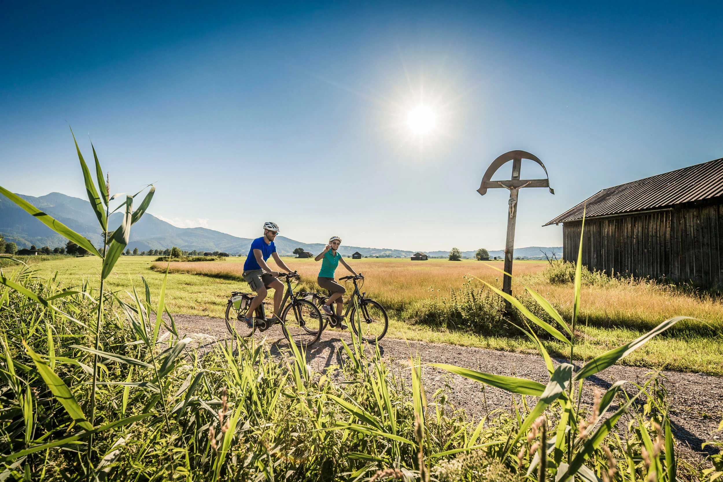 Deutschland © Tourist Information Kochel am See - Thomas Kujat Zwei Radfahrer auf Landweg bei sonnigem Wetter vor Berglandschaft