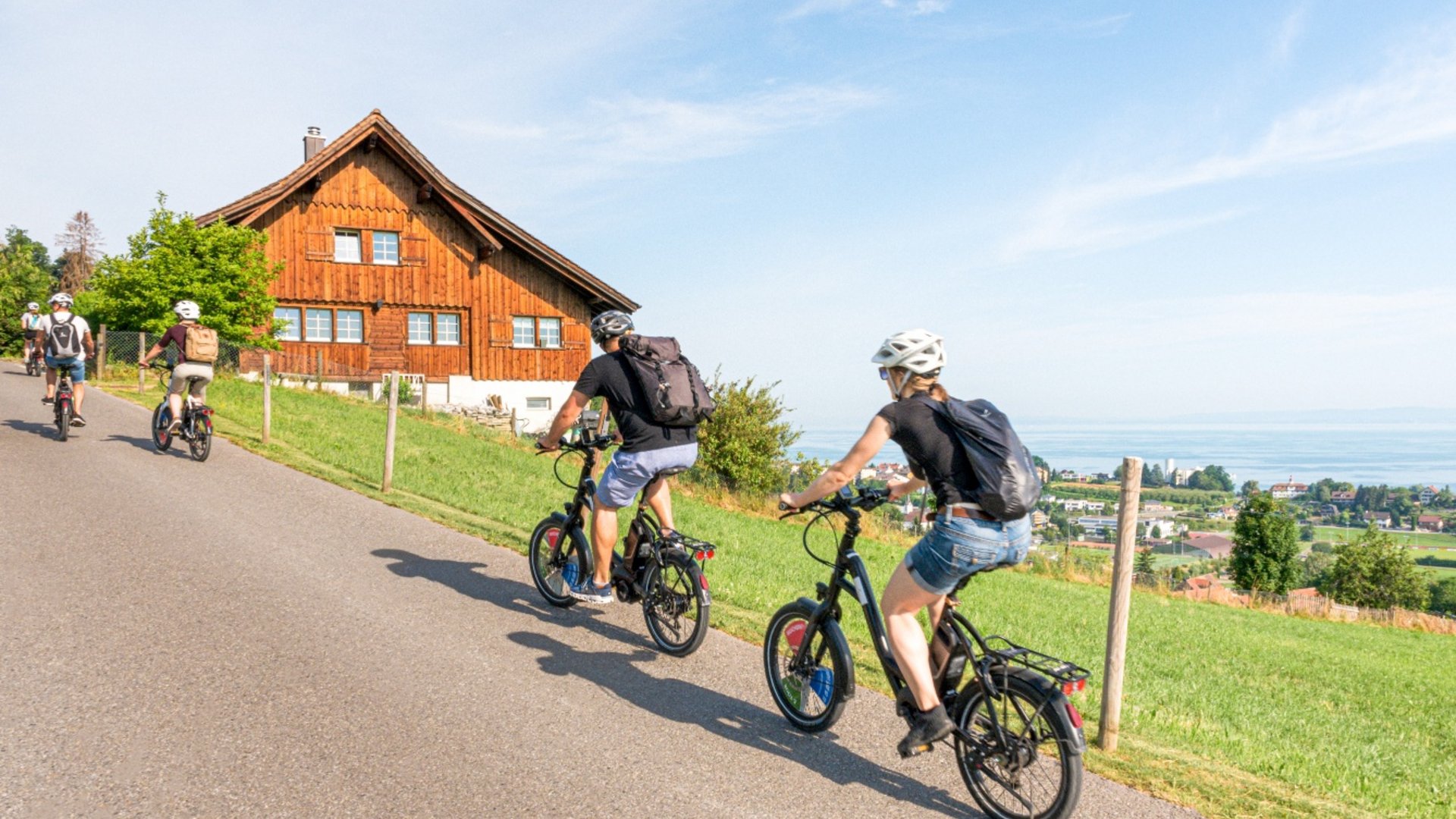 Group riding e-bikes on country road near wooden house and green field