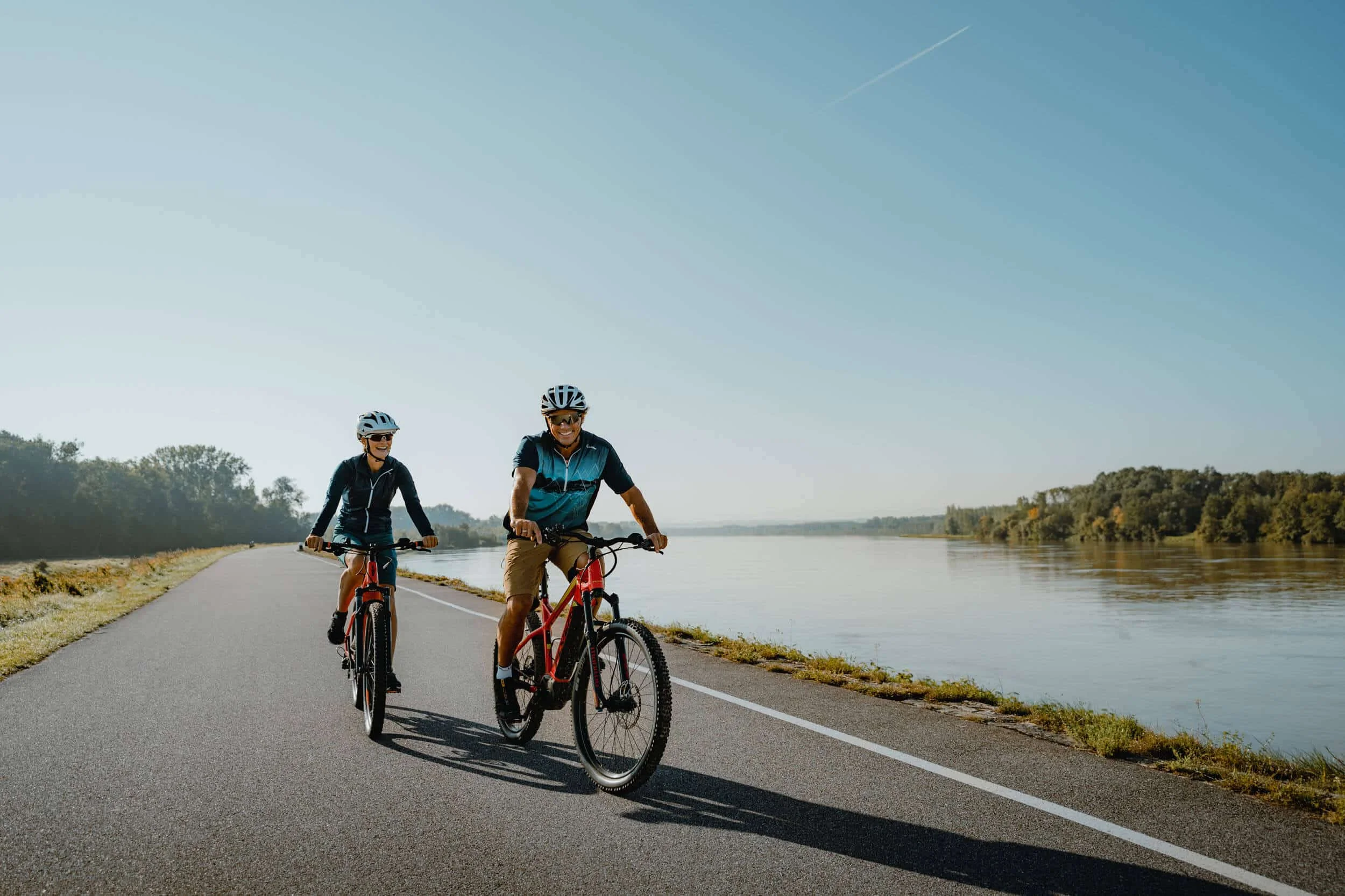 Fietspaden voor lange afstanden © WGD Donau Oberösterreich Tourismus GmbH CM Visuals Twee personen fietsen op een pad naast een rivier op een zonnige dag