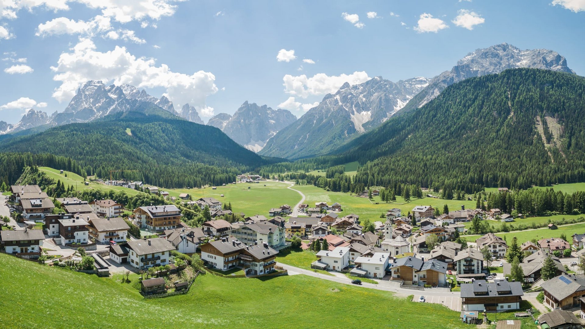 Village in valley with mountains and forests under blue sky