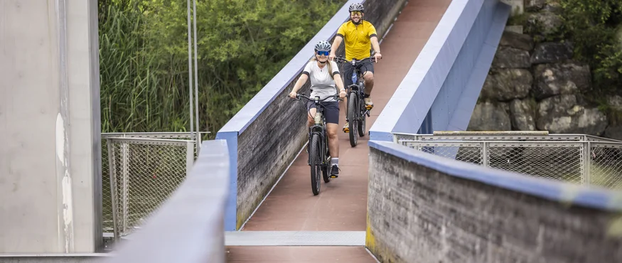 Zwei Radfahrer auf einer schmalen Brücke von Bäumen umgeben