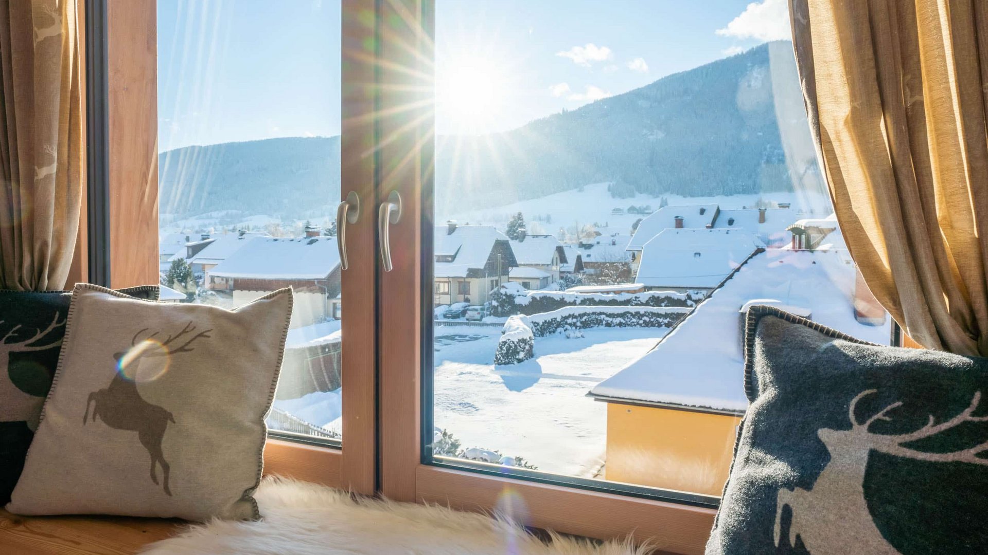 Sunny view of snowy houses and mountains through window with reindeer pillows