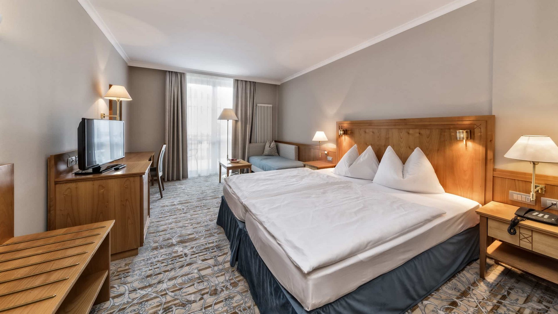 Bright hotel room with double bed, TV, and seating area