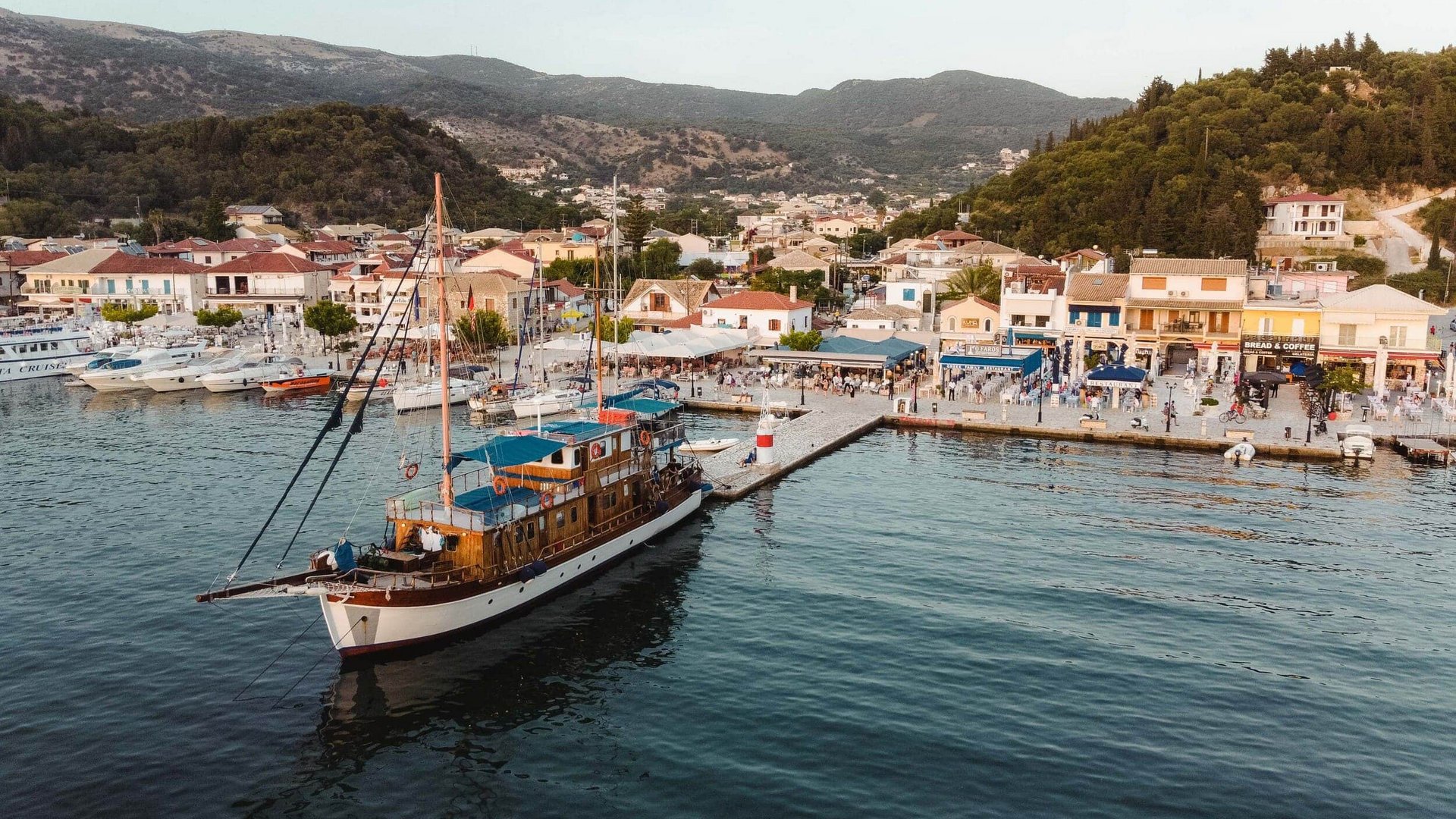 Sailboat docked at a busy harbor with mountainous landscape
