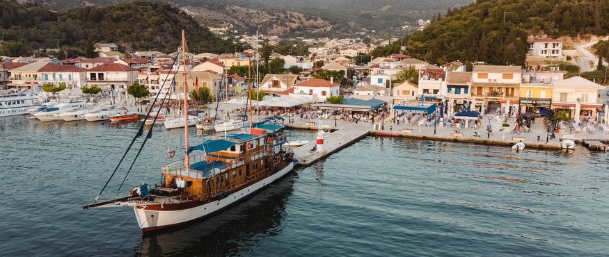 Sailboat docked at a busy harbor with mountainous landscape
