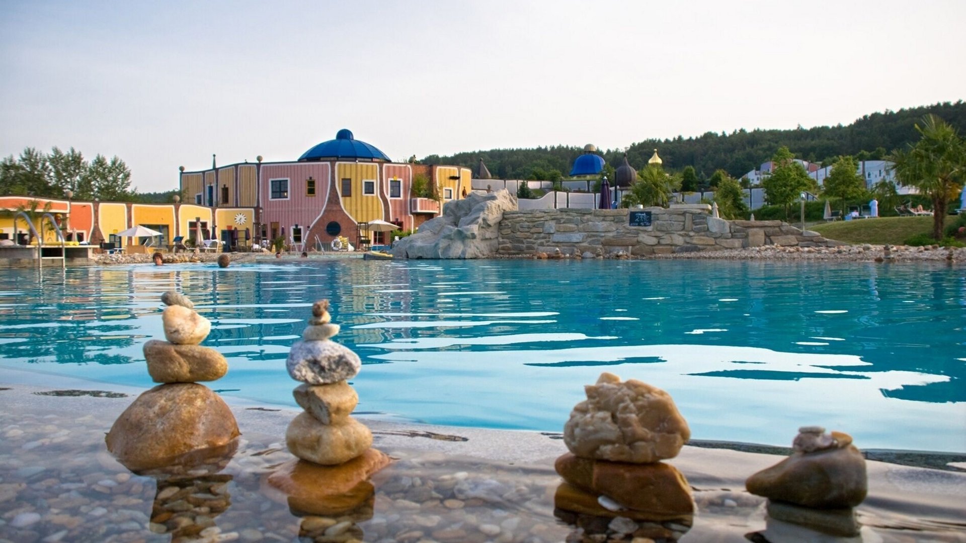 Stacked stones by pool edge with colorful building and trees behind