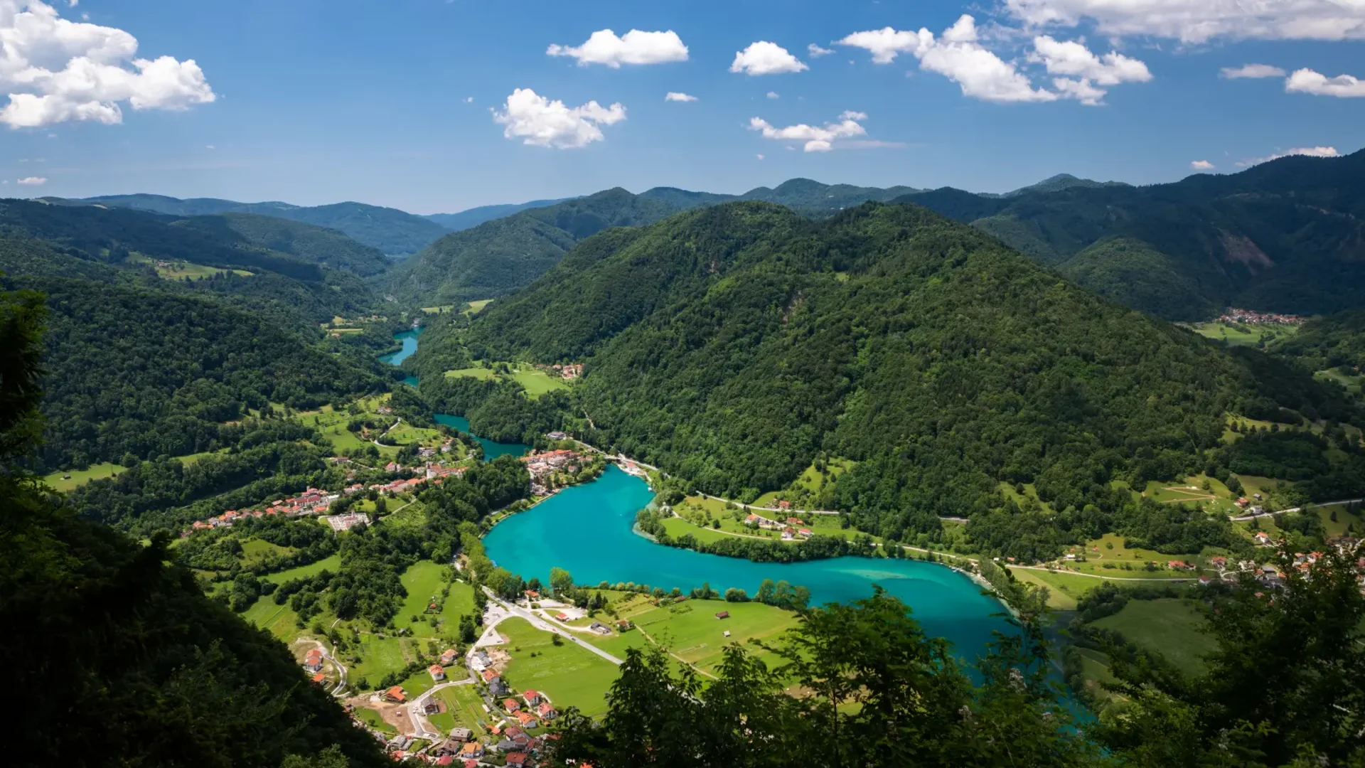 Rivier kronkelt door groen dal met bergen en dorpen onder blauwe lucht
