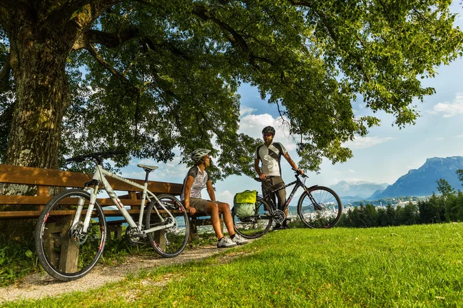 Velontour © Markus Greber Zwei Radfahrer machen Pause auf einer Bank unter einem Baum mit Bergblick