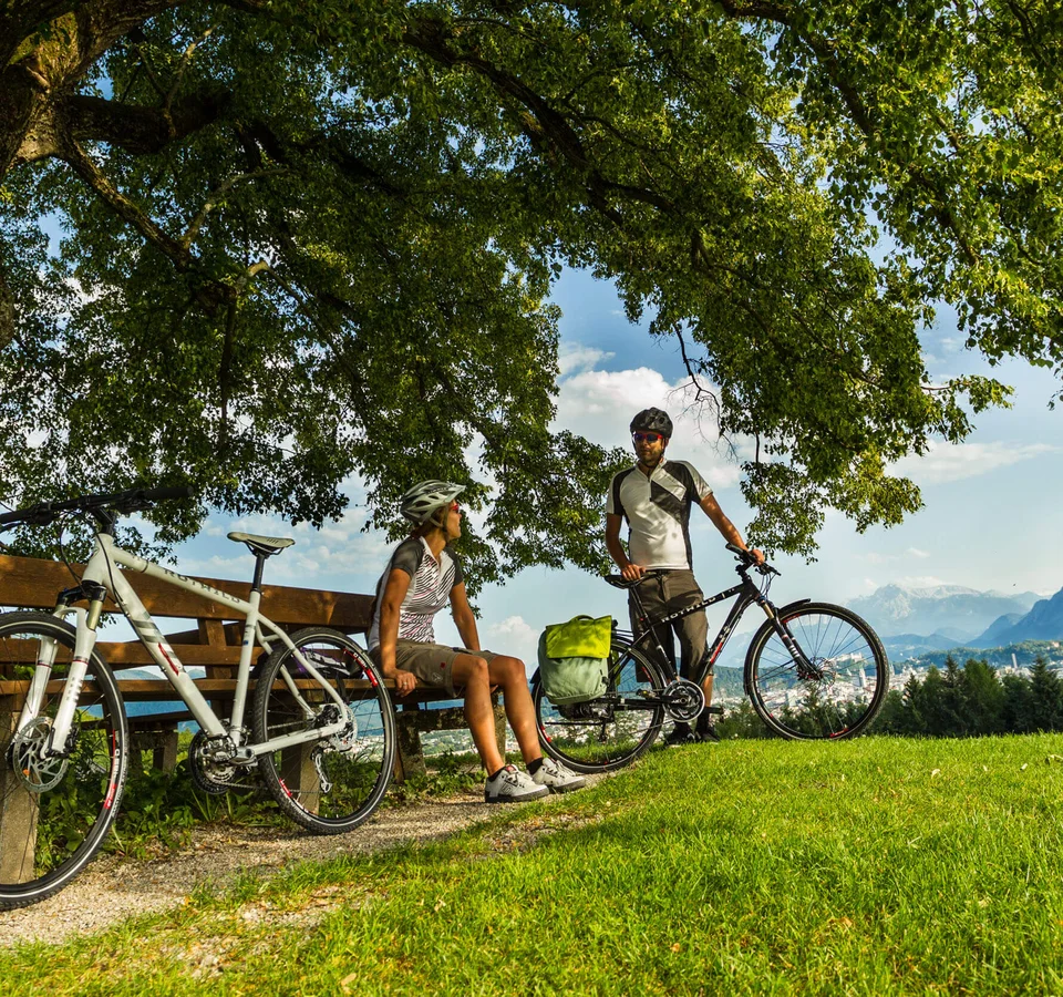 Anthering: Radurlaub zwischen Moor & Mozartstadt © Markus Greber Zwei Radfahrer machen Pause auf einer Bank unter einem Baum mit Bergblick