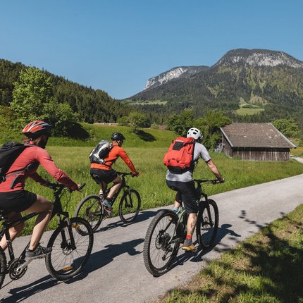 Three cyclists biking on rural path with mountains and greenery around