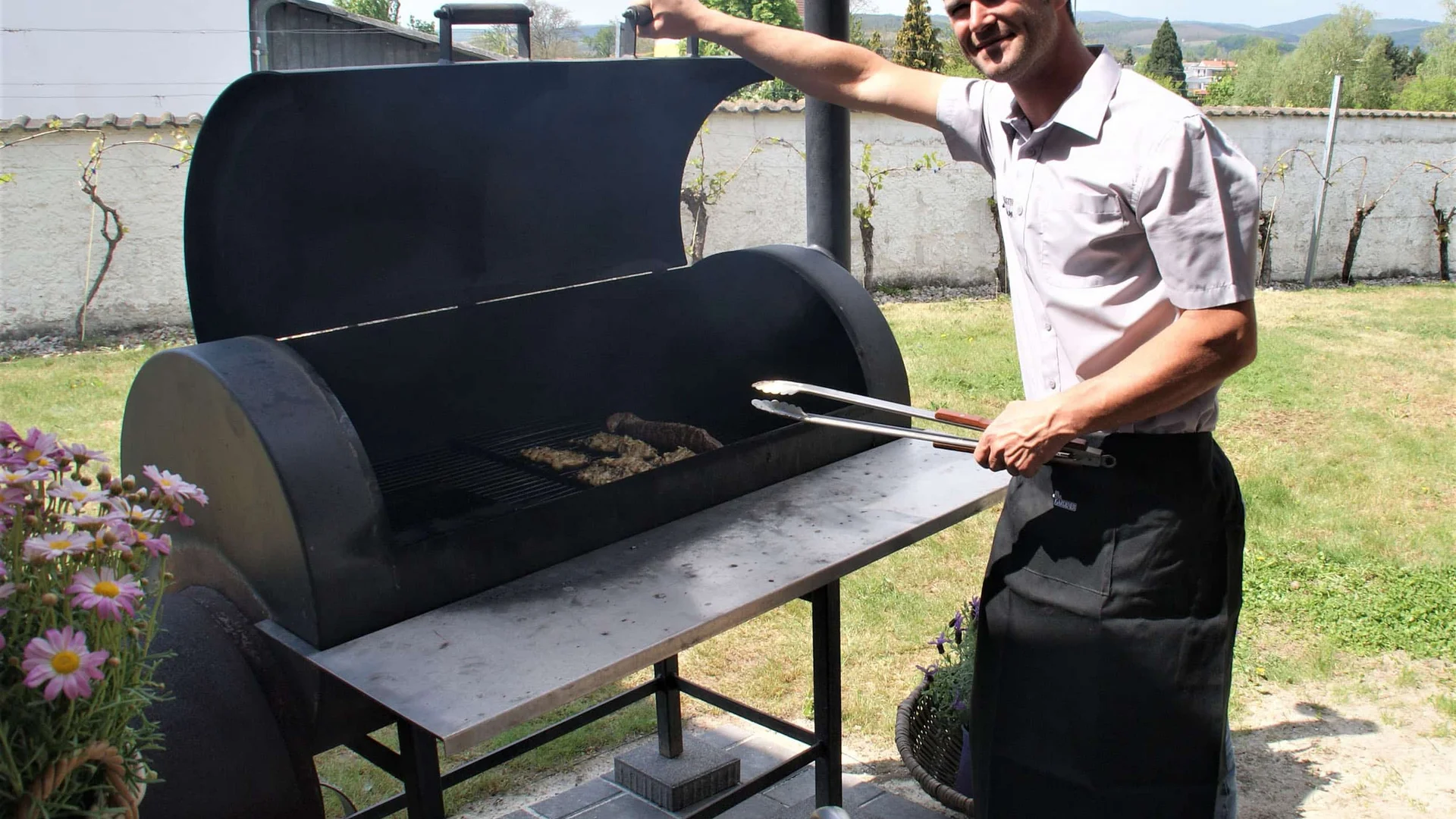 Man die worsten en vlees bakt op een grote barbecue in de tuin
