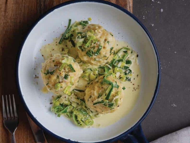 Three dumplings with cream sauce and chives in pan on wooden board
