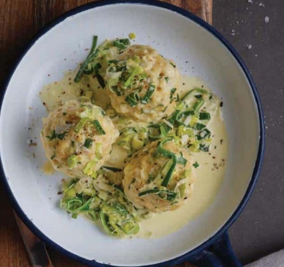 Three dumplings with cream sauce and chives in pan on wooden board