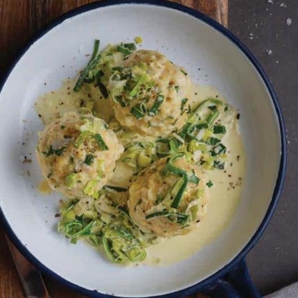 Three dumplings with cream sauce and chives in pan on wooden board