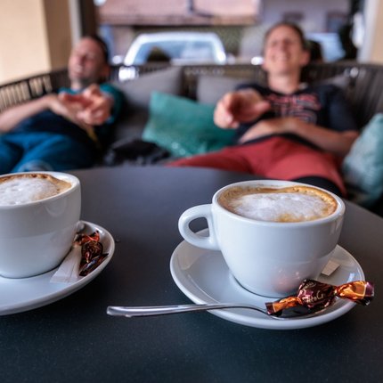 Two cups of cappuccino on a table with two relaxed people in the background
