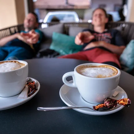 Twee kopjes cappuccino op een tafel met twee ontspannen personen op de achtergrond