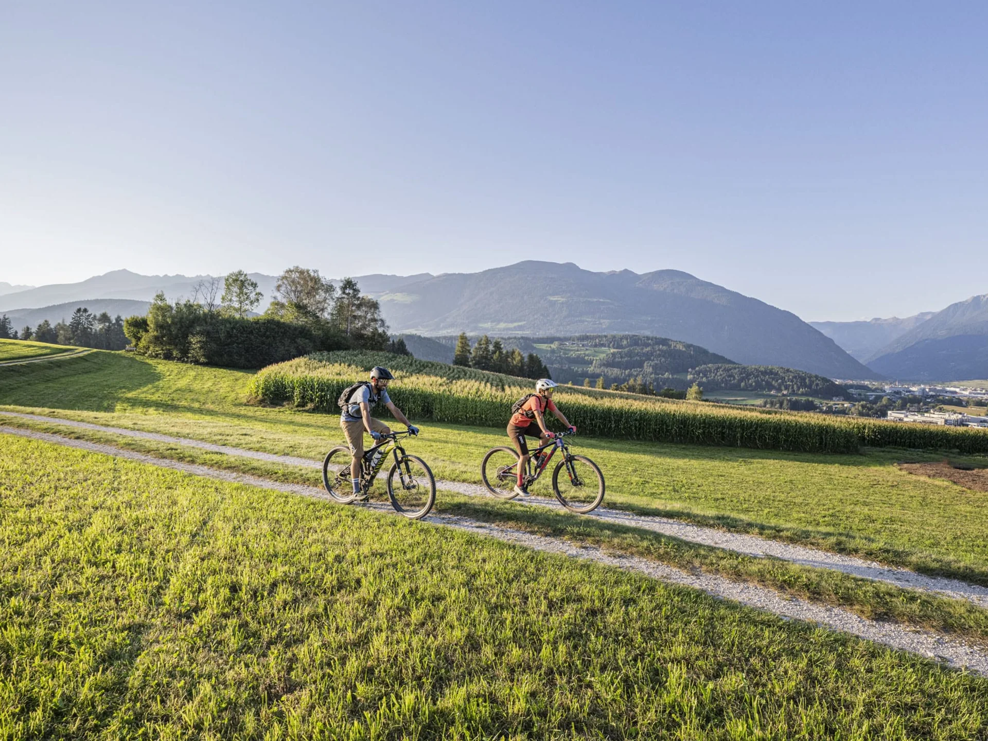 Twee fietsers op een pad door groene velden met bergen op de achtergrond