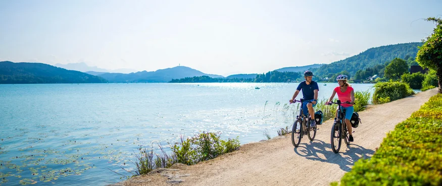 Twee fietsers op een pad langs het meer met bergen op de achtergrond