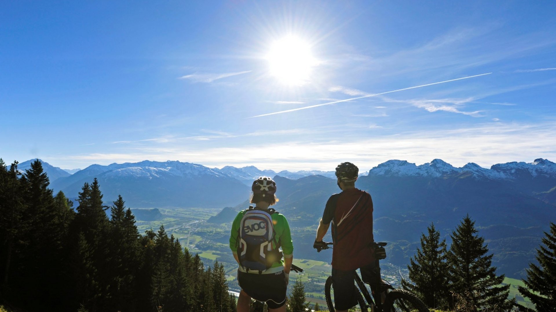 Two mountain bikers overlooking mountains and valley under bright sun
