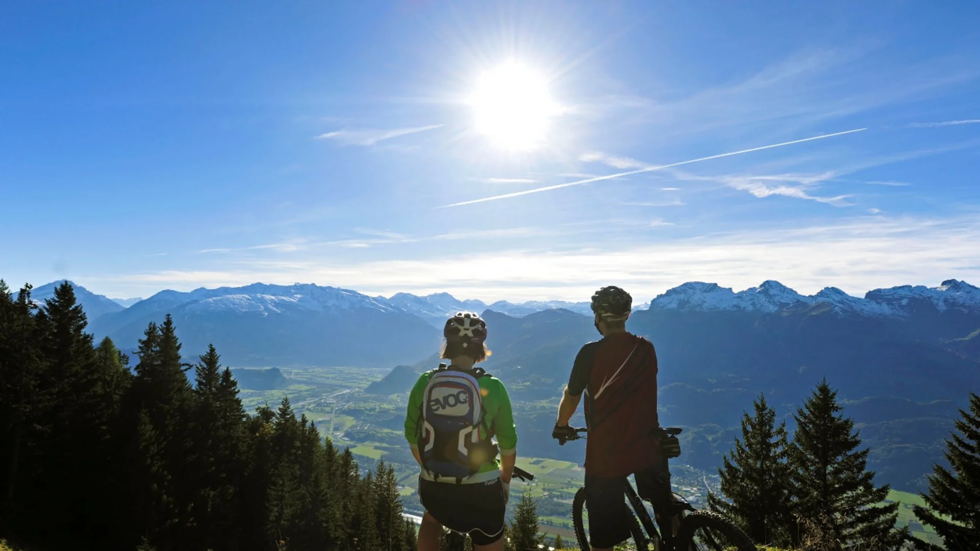Zwei Mountainbiker genießen die Aussicht auf Berge und Tal bei Sonnenschein