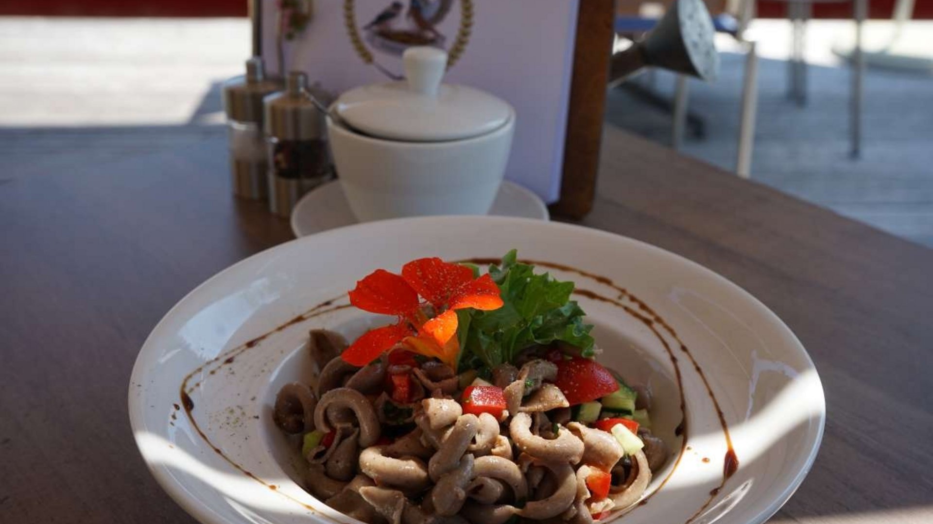 Bowl of pasta salad garnished with flowers and greens on wooden table