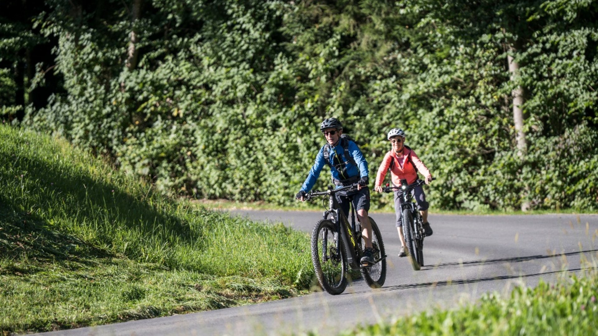 Twee fietsers fietsen op een weg naast groene struiken en gras