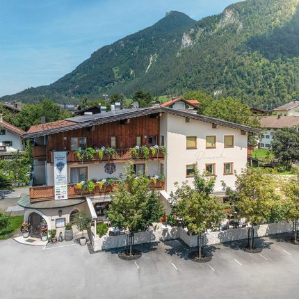 Guesthouse with mountain backdrop and trees in sunny valley