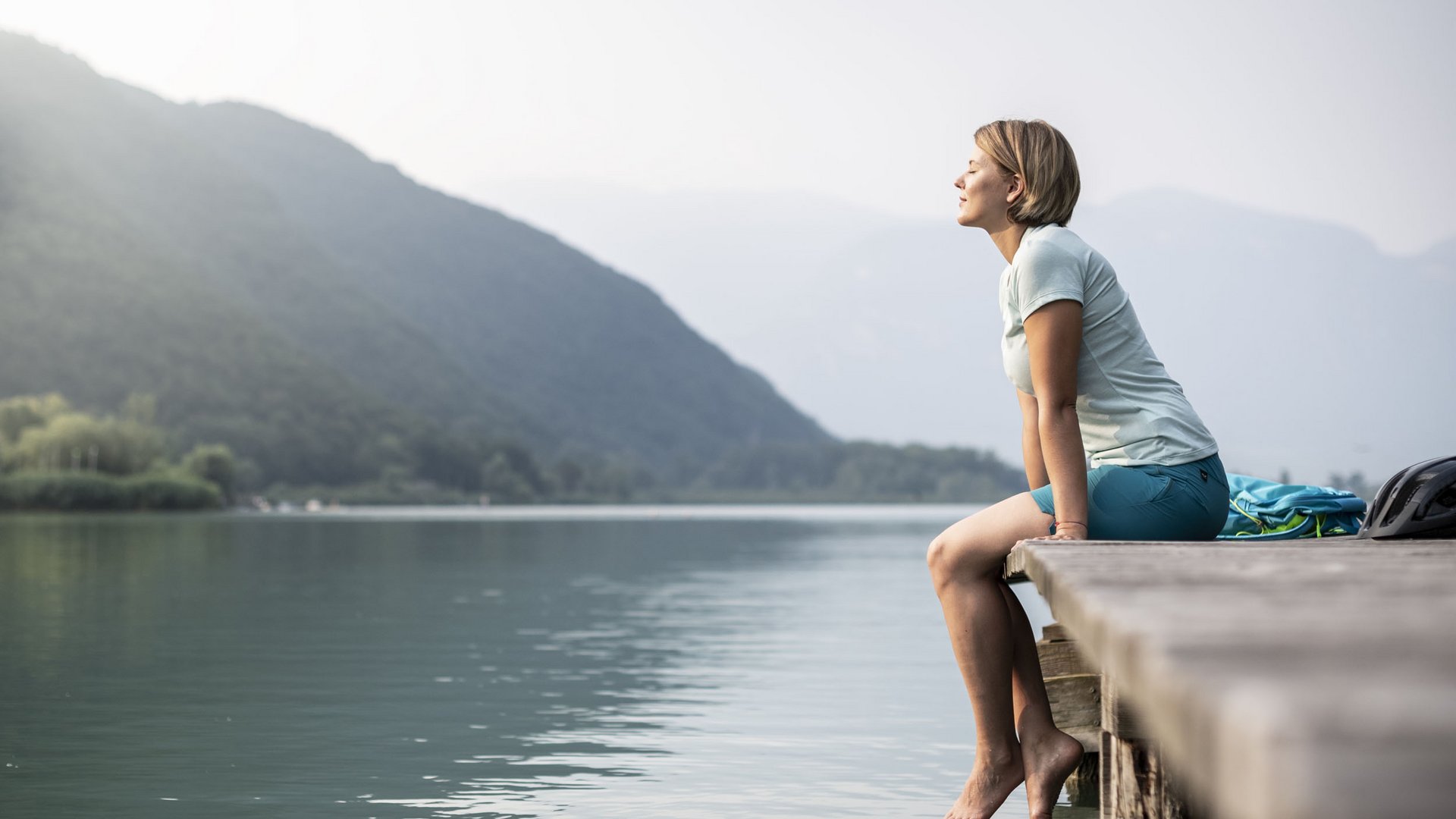 Woman sitting relaxed on wooden dock at lake with mountains