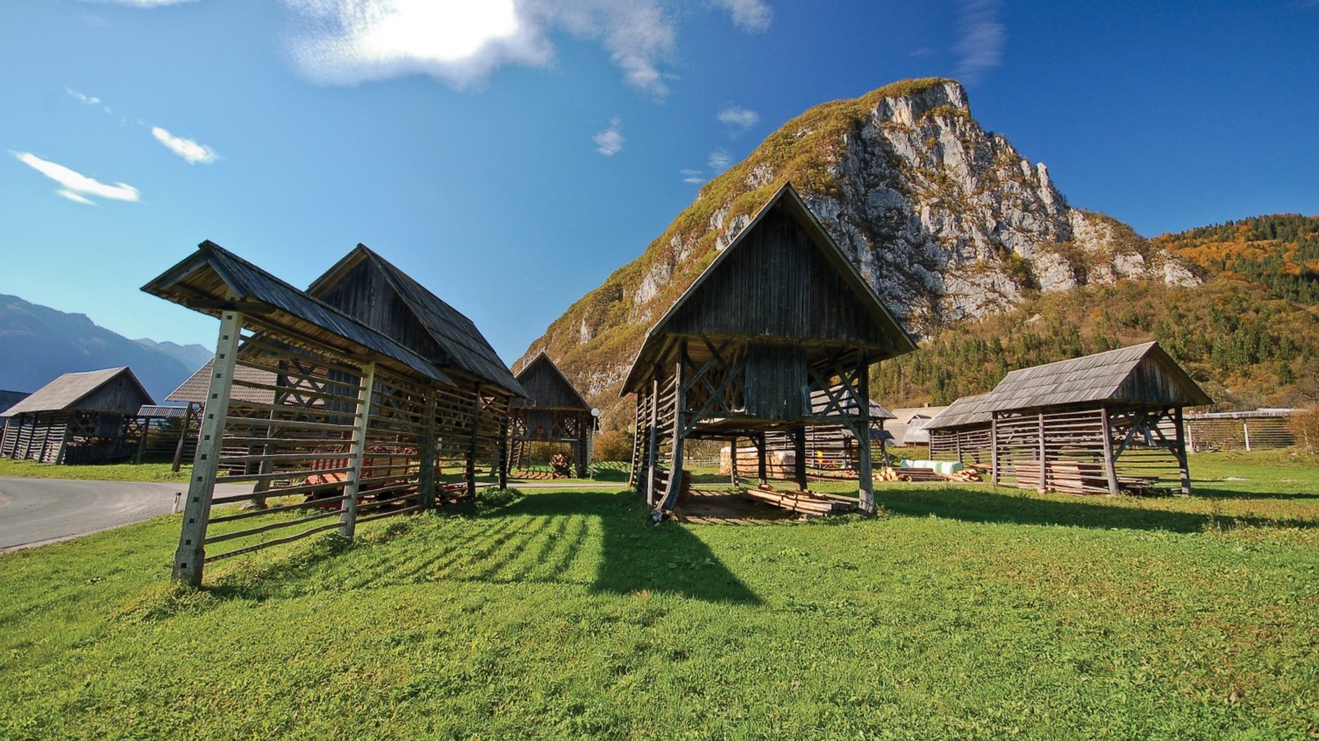 Wooden barns on green grass with rocky mountain and blue sky background