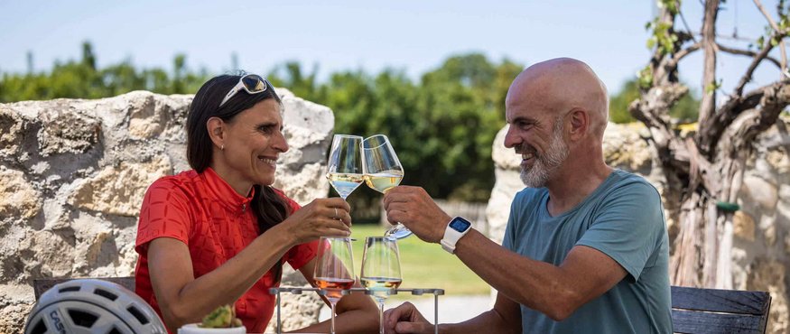 Couple toasting white wine outdoors sitting at wooden table with snacks