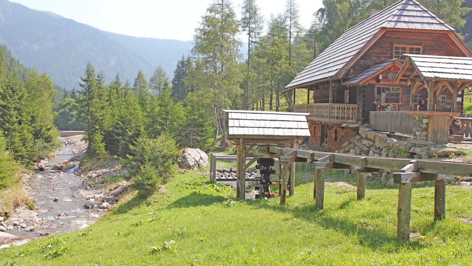 Wooden mill by stream in green mountain landscape