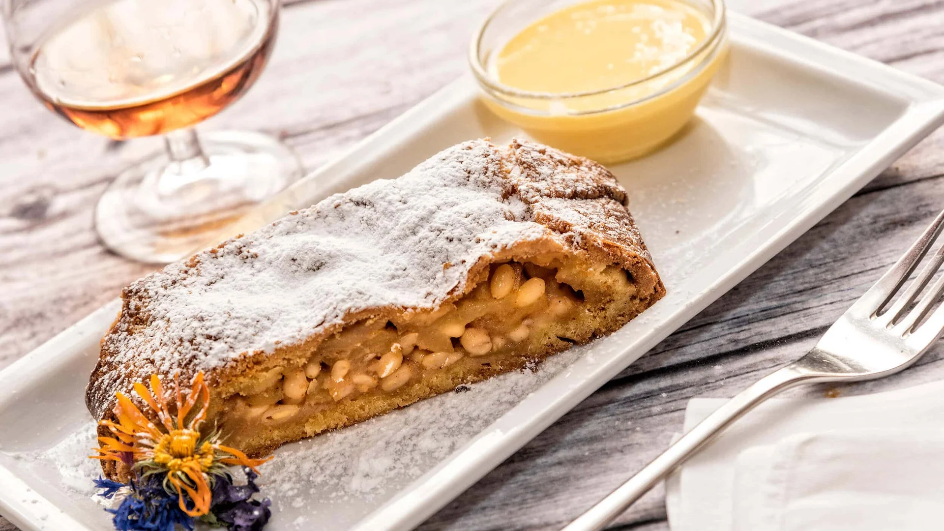 Stuk cake met poedersuiker, notenvulling en vanillesaus op wit bord