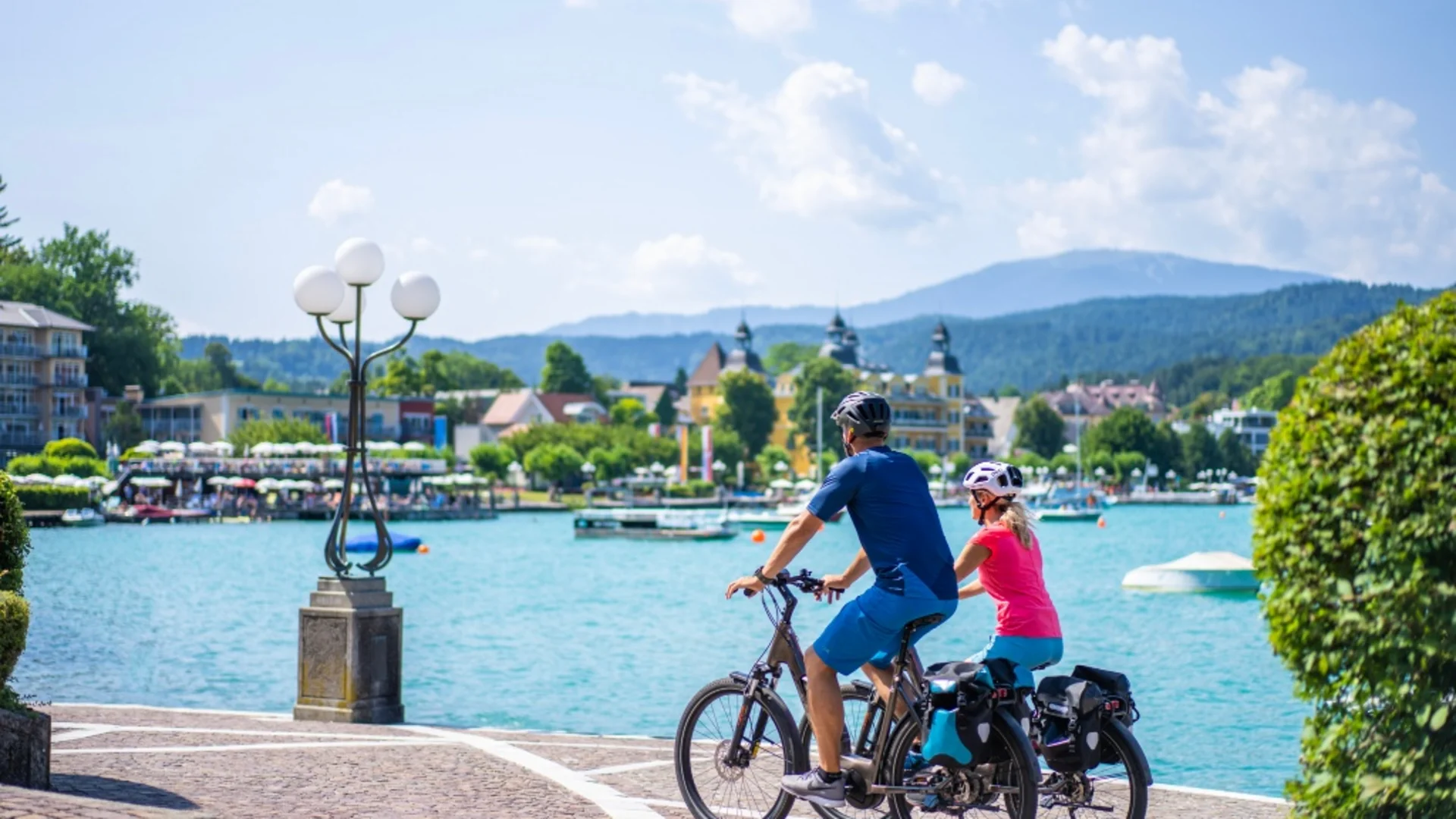 Twee fietsers bij het meer met bergen en gebouwen op de achtergrond