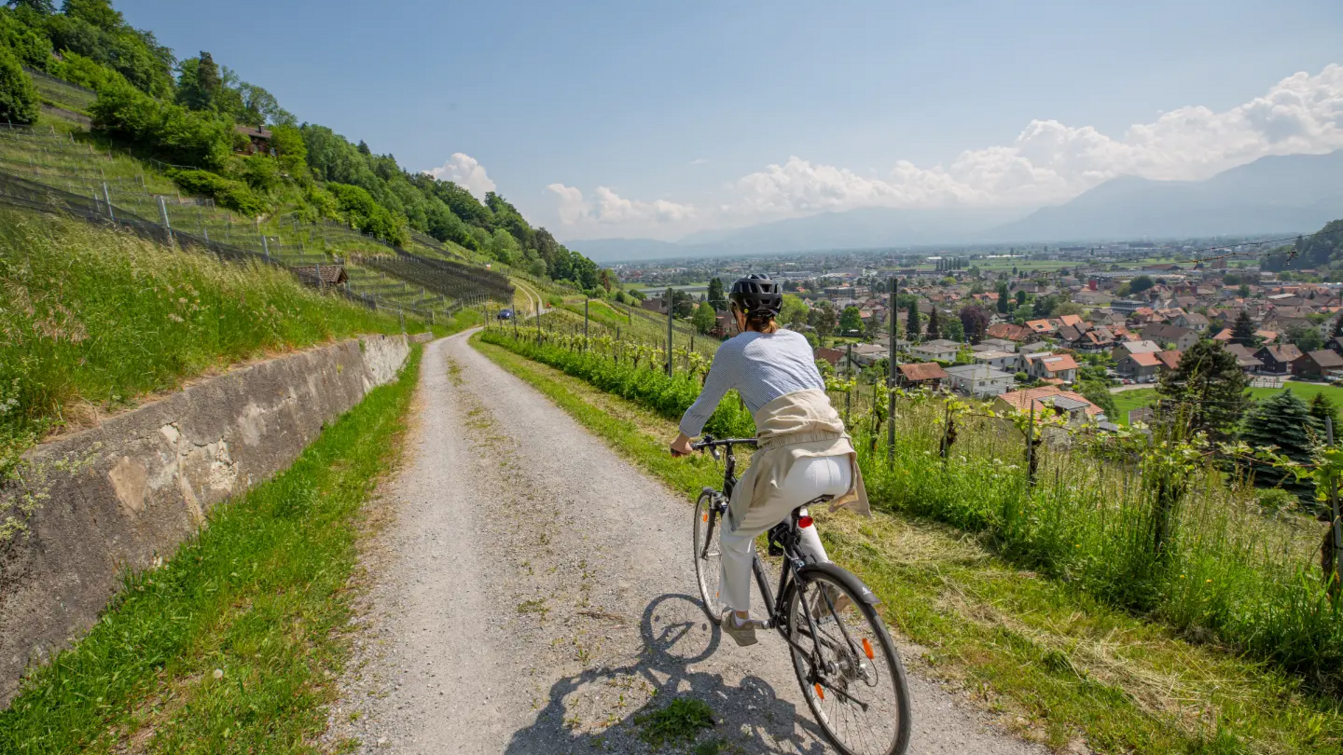 Woman cycling on rural path overlooking town and mountains