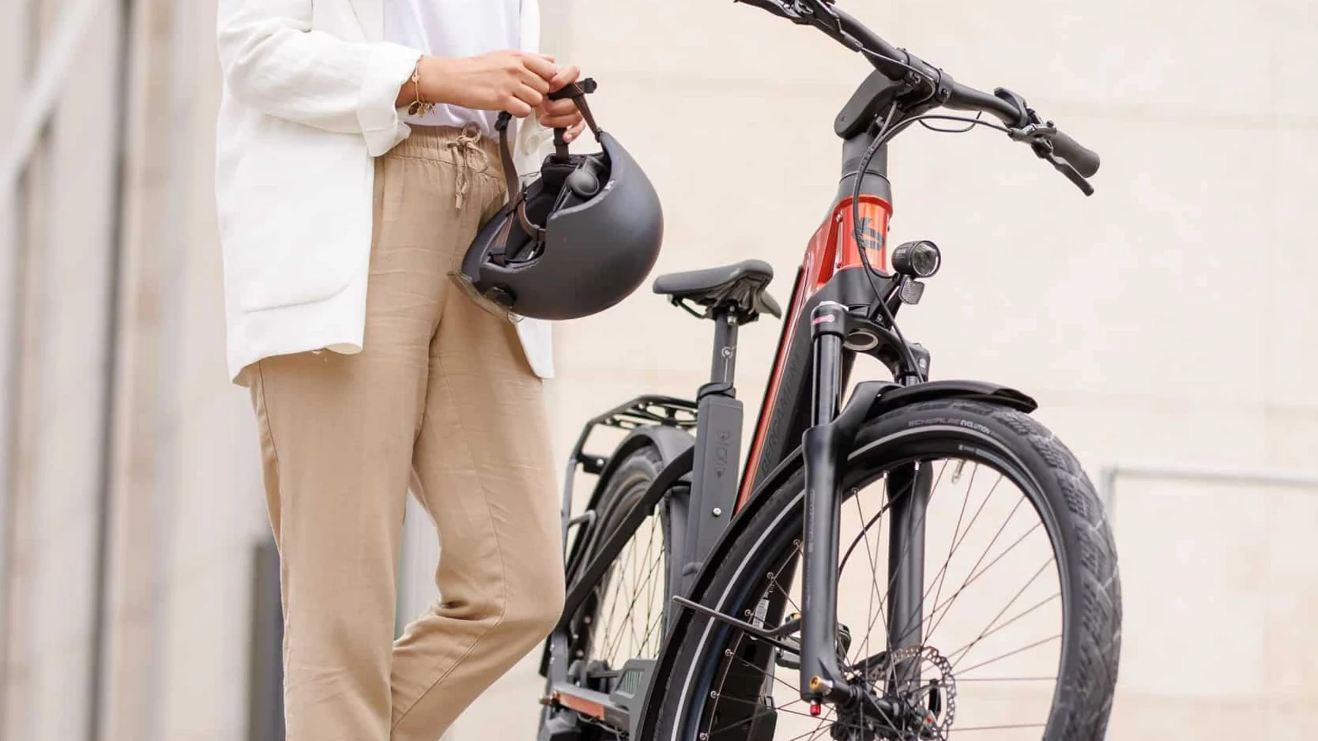 Schwalbe © Ralf Bohle GmbH Vrouw met helm staat naast rode elektrische fiets voor gebouw