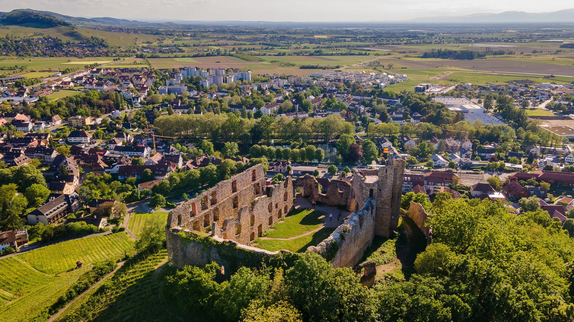 Aerial view of a castle ruin above a town and green fields