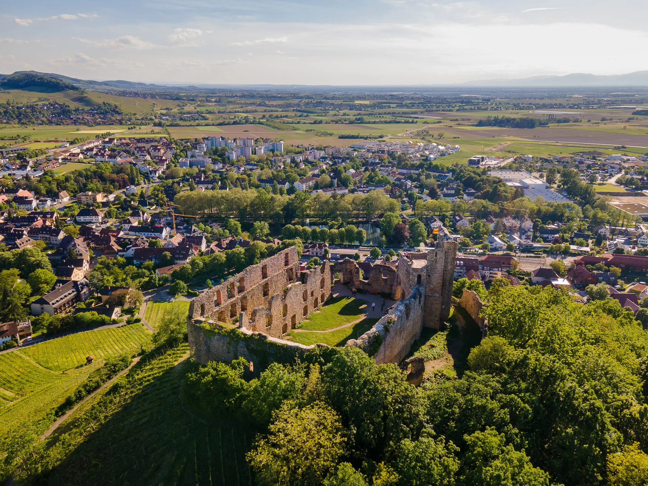 Luftaufnahme einer Burgruine über einer Stadt und grünen Feldern