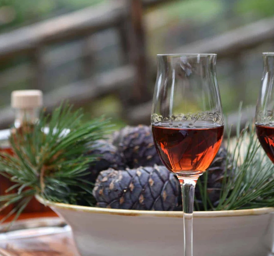 Twee glazen met donkere drank bij een bord met dennenappels en groene takken
