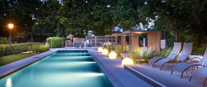 Garden & Spa Hotel das Götzfried **** © Michael Huber Fotographie Verlichte buitenzwembad met ligstoelen en cabana's bij schemering