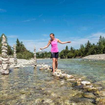 Woman barefoot balancing on stones in river with stacked stone pillars nearby
