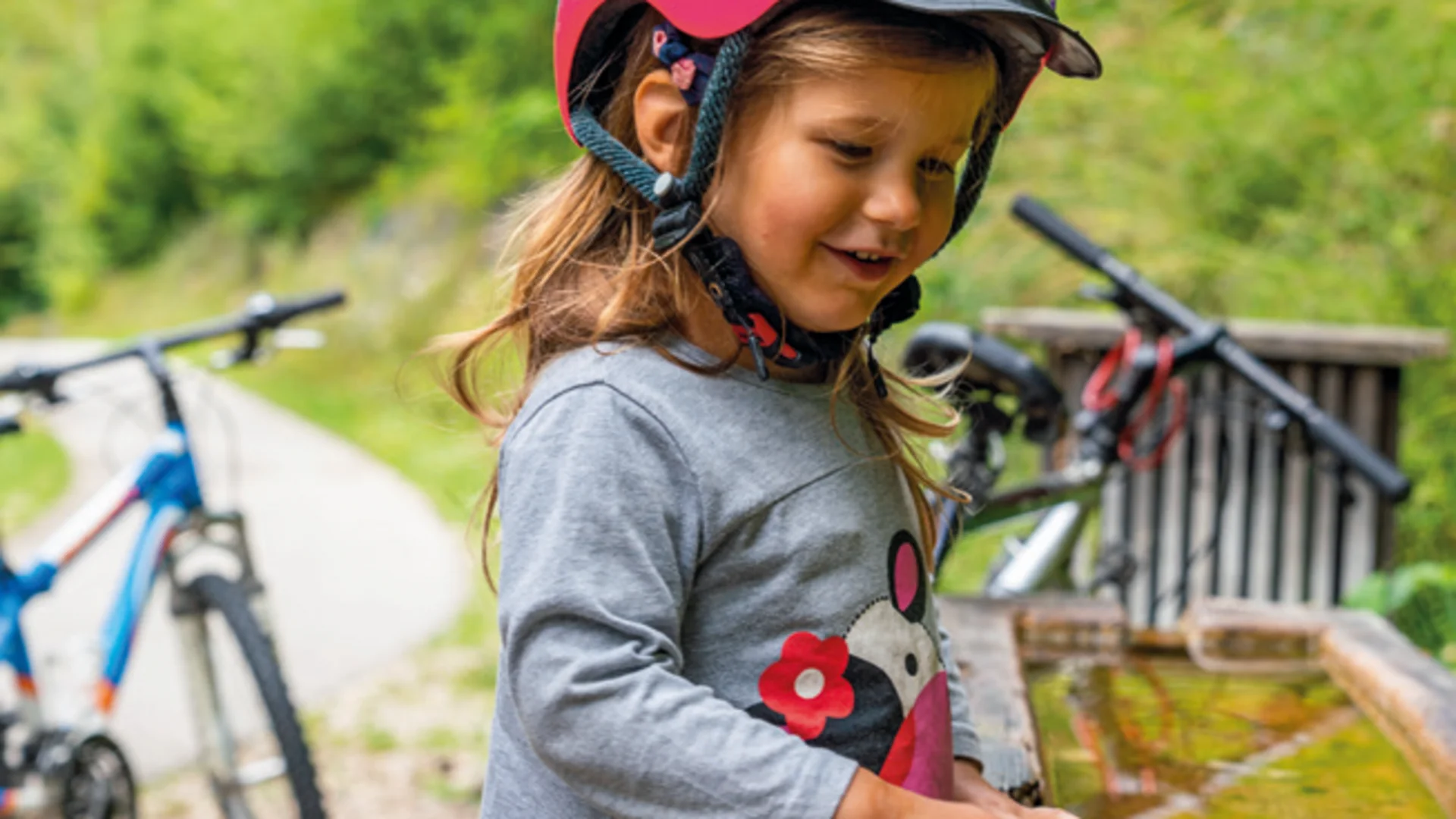 Kind met fietshelm raakt water aan bij een fontein in het bos