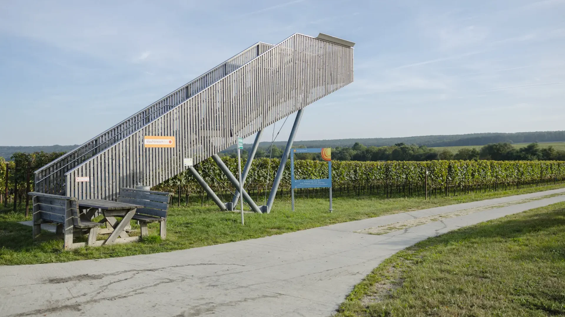 Tour-Detail © wearegiving Holz-Aussichtsturm mit Sitzbank neben Weinbergen und Weg