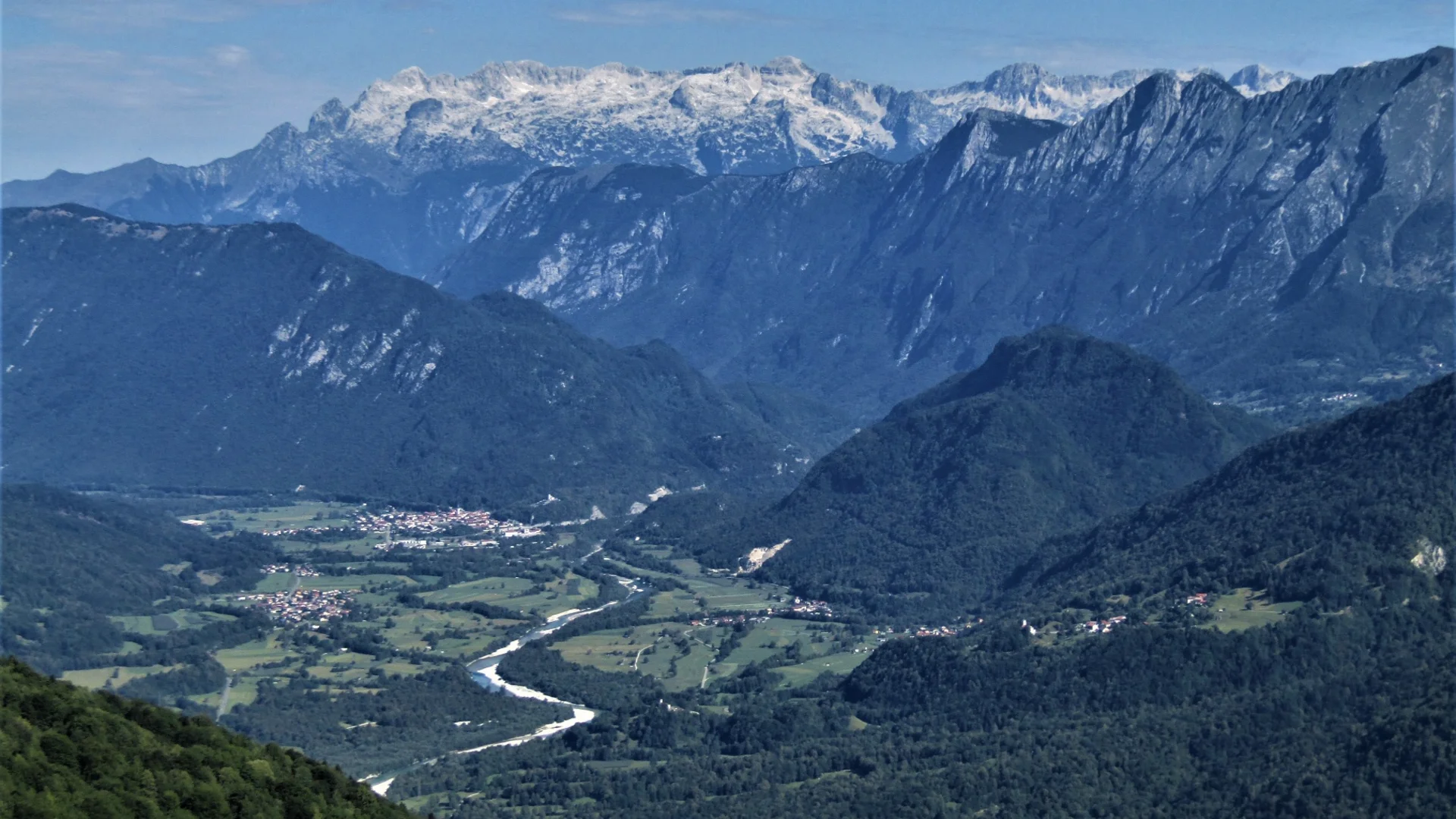Uitzicht op een groene vallei met rivier en besneeuwde bergen op de achtergrond