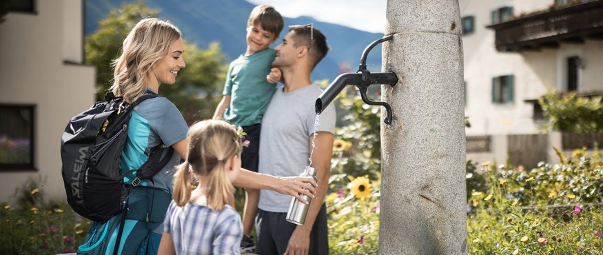 Family filling bottle at fountain in mountain village