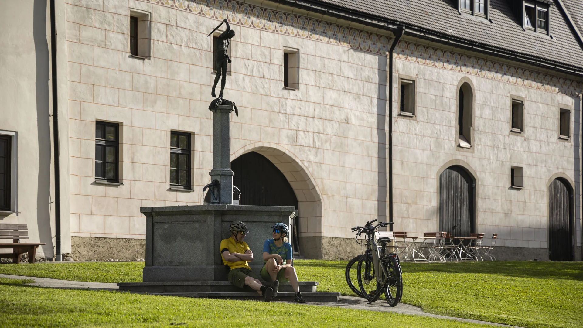 Radfahren ohne Höhenmeter-Stress im Quellenviertel © Velontour - Heiko Mandl Zwei Radfahrer sitzen an einer Statue vor einem historischen Gebäude