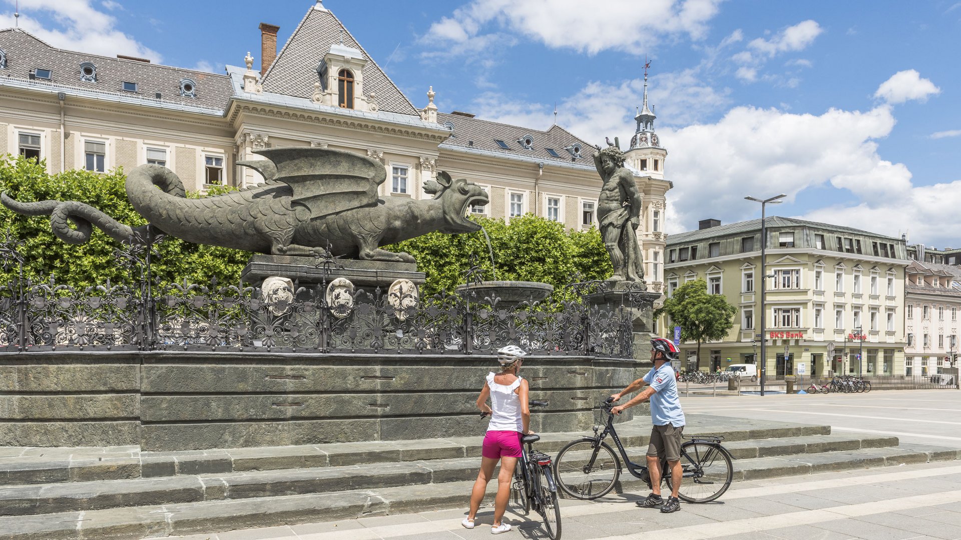 Two cyclists viewing the Lindwurm fountain in Klagenfurt