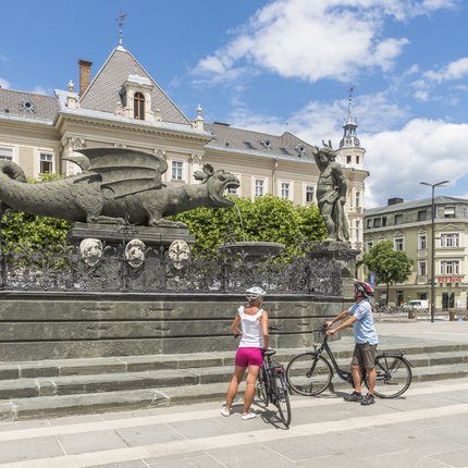 Two cyclists viewing the Lindwurm fountain in Klagenfurt
